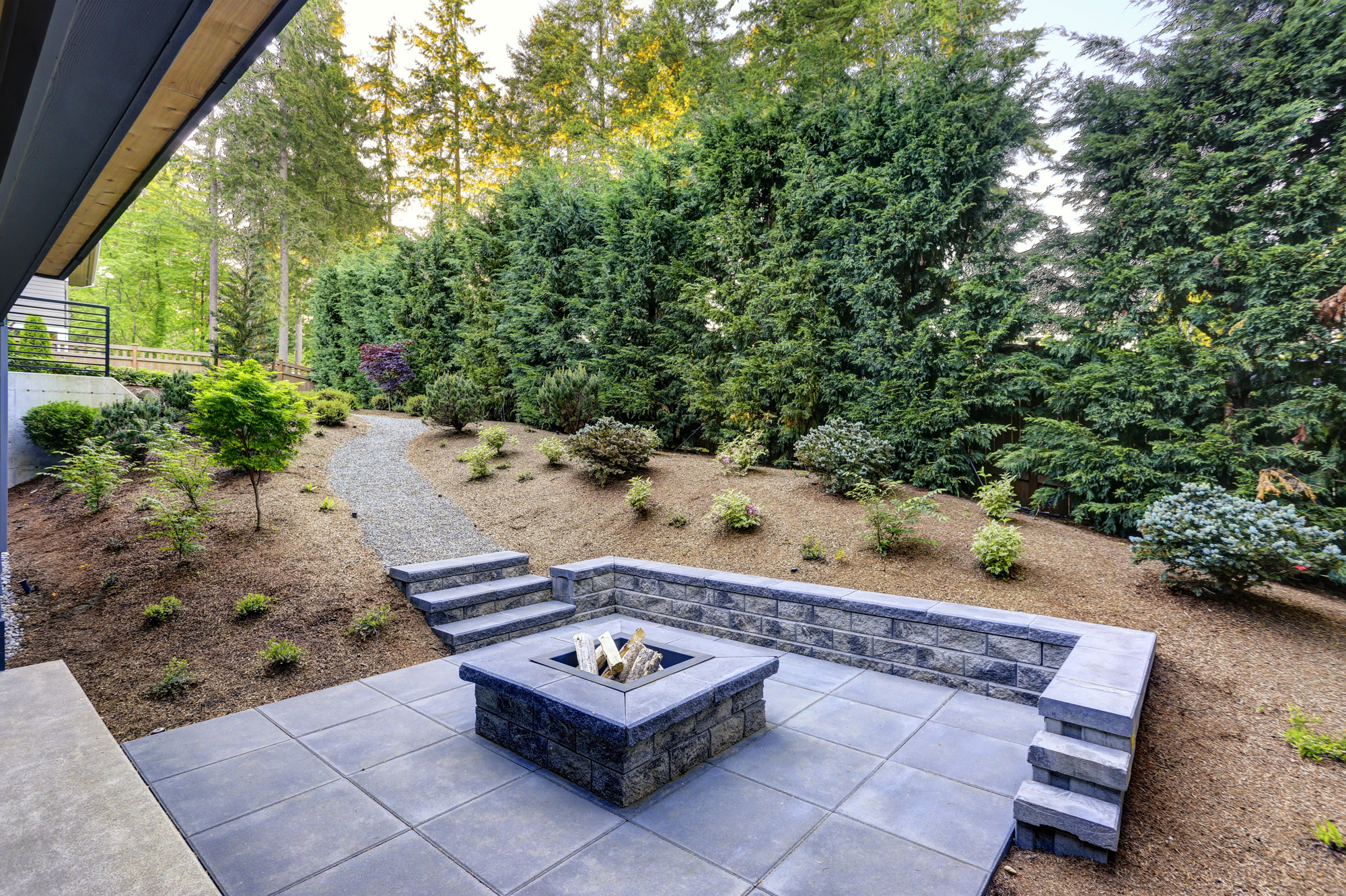 New modern home features a backyard with rectangular concrete fire pit framed by slate pavers and overlooking the lush garden. Northwest, USA
